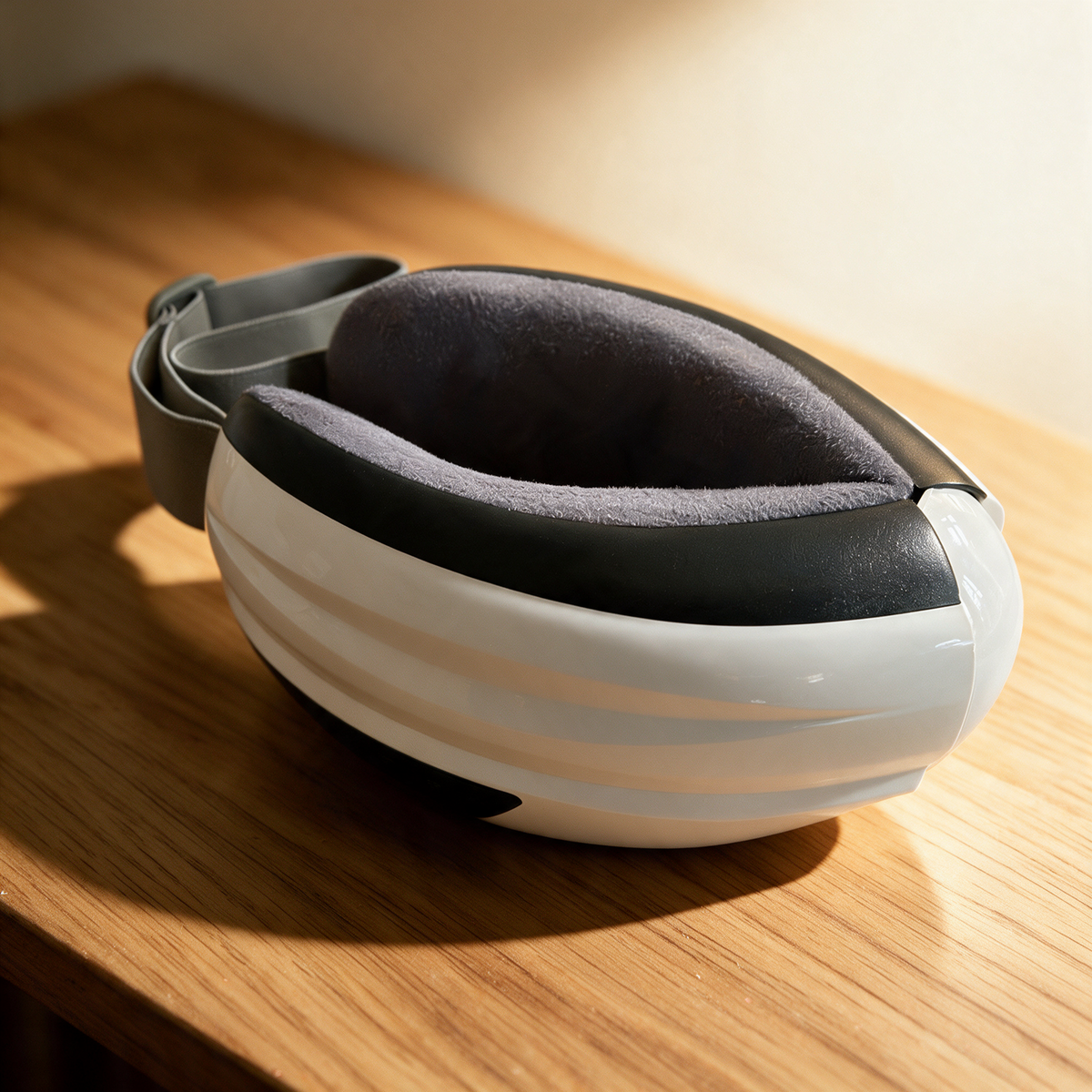 The Nove Body Heated Eye Massager folded up, on an oak table
