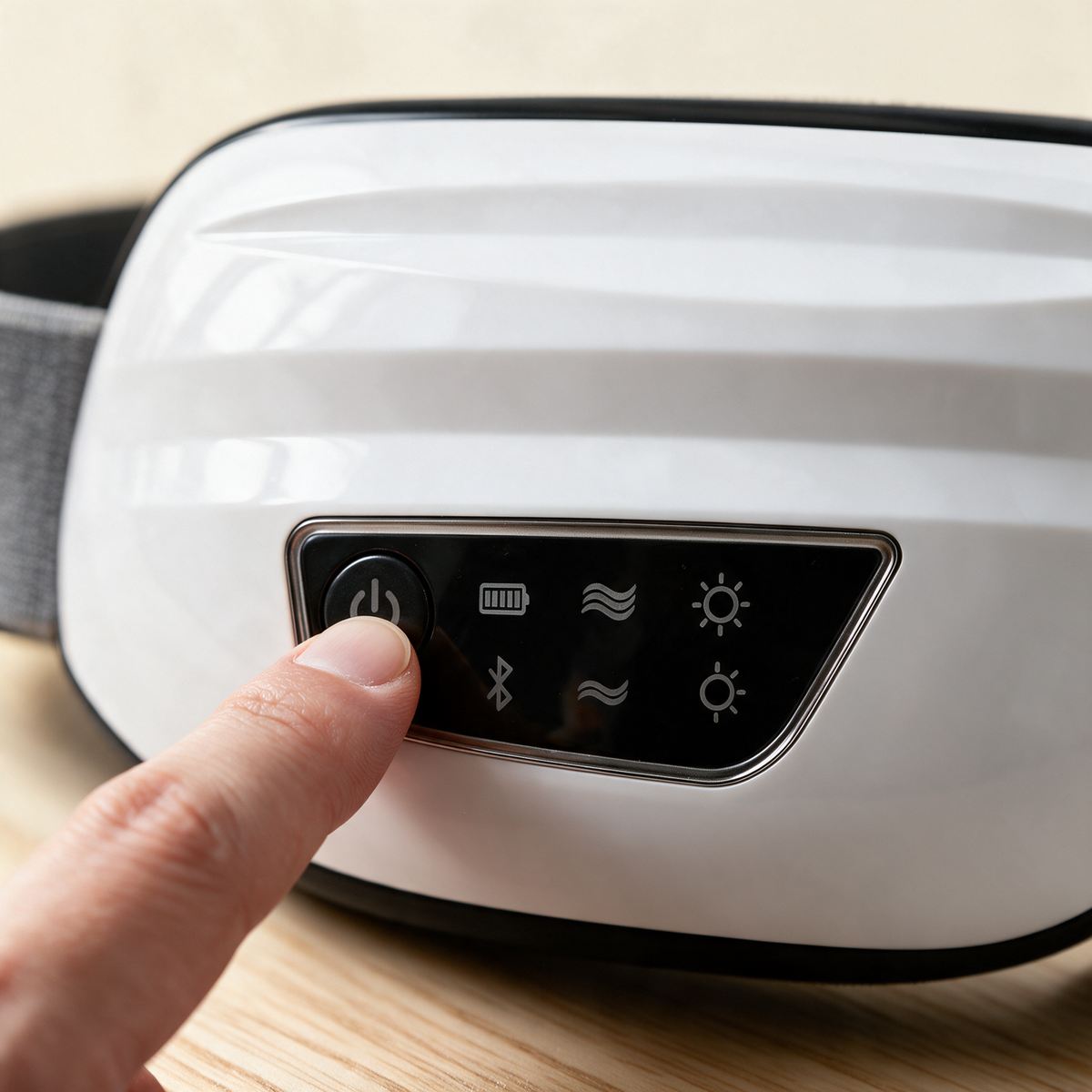 A fingertip on the power button of the Nove Body Heated Eye Massager, with every light switched off